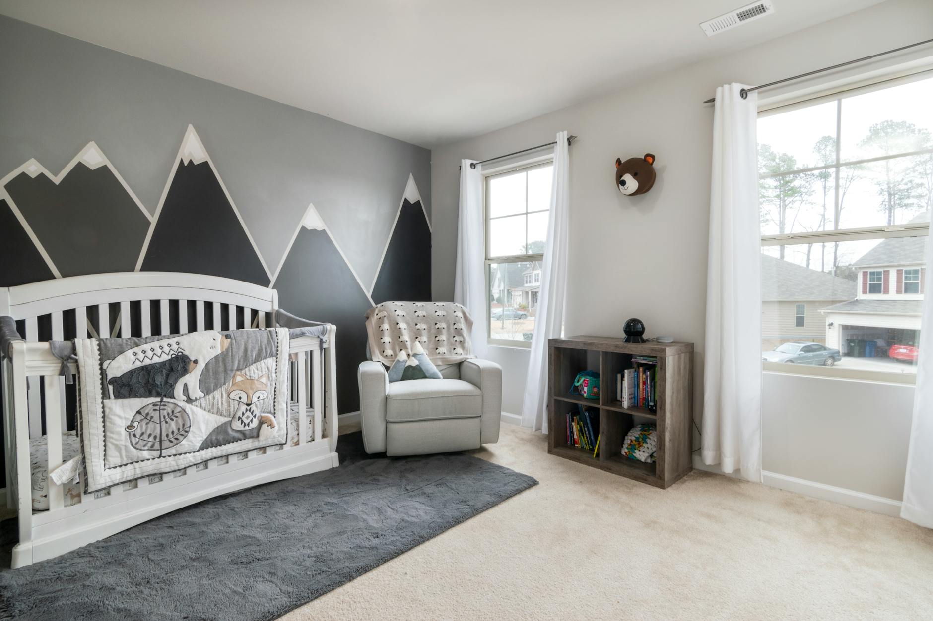 Stylish nursery room featuring mountain mural, comfortable reading chair, and cozy crib setup with soft natural light