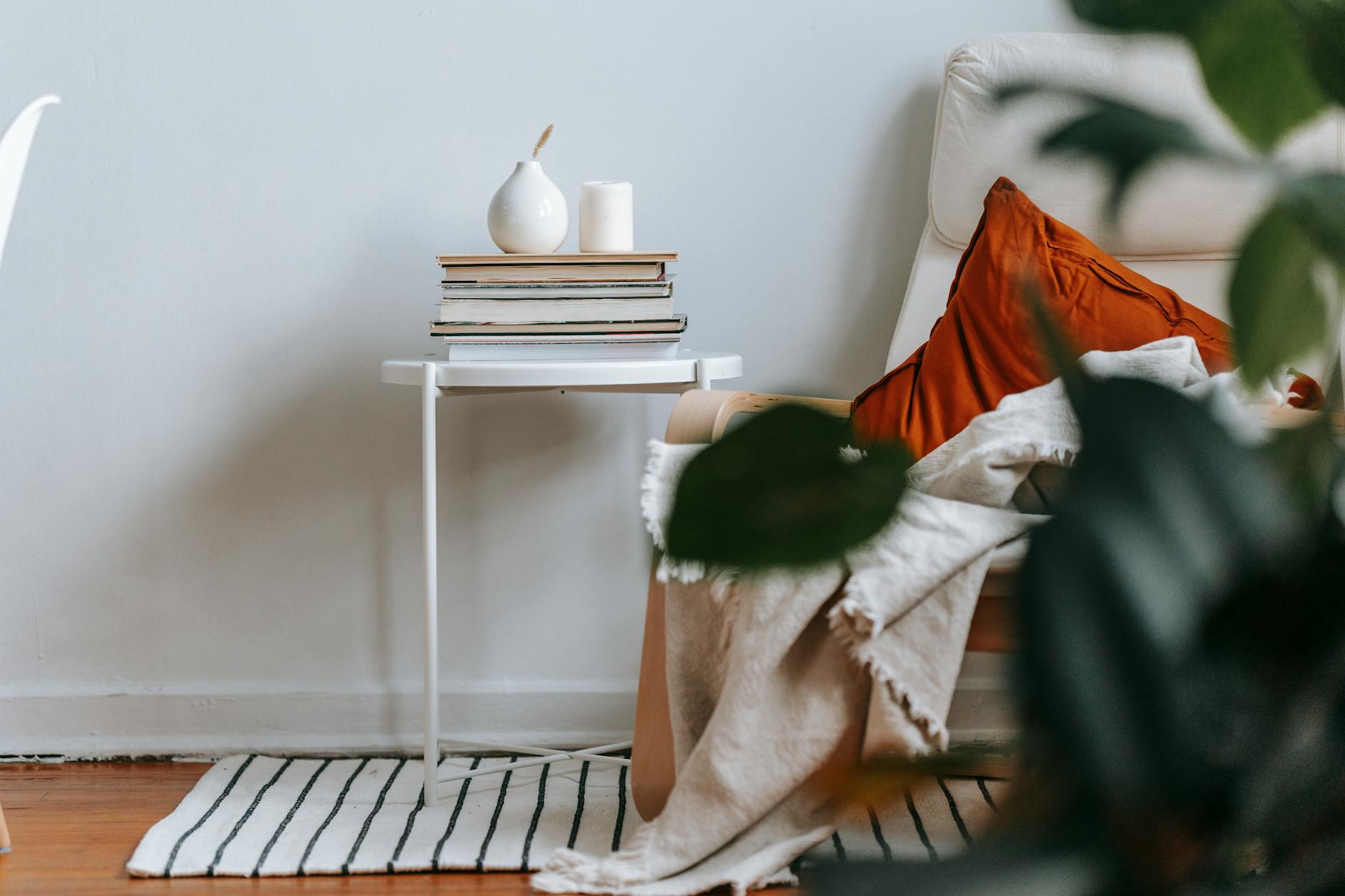 A warm, minimal reading nook with a cushioned armchair, plaid throw, stack of books, and a ceramic vase in soft natural light