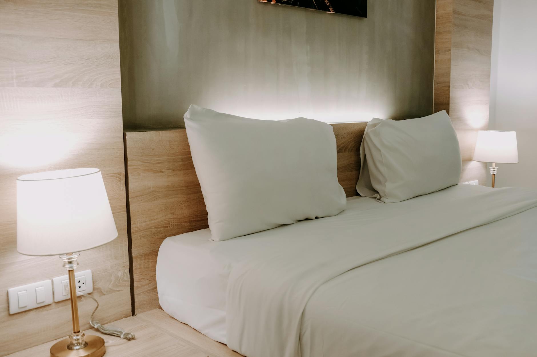 Minimal bedroom with neutral bedding, warm ambient lighting, and a clean wall ready to be made intentional