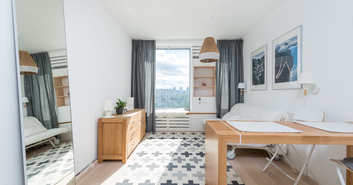 Wooden table and drawer placed in room with big window and wall decorated with pictures in light room with mirror