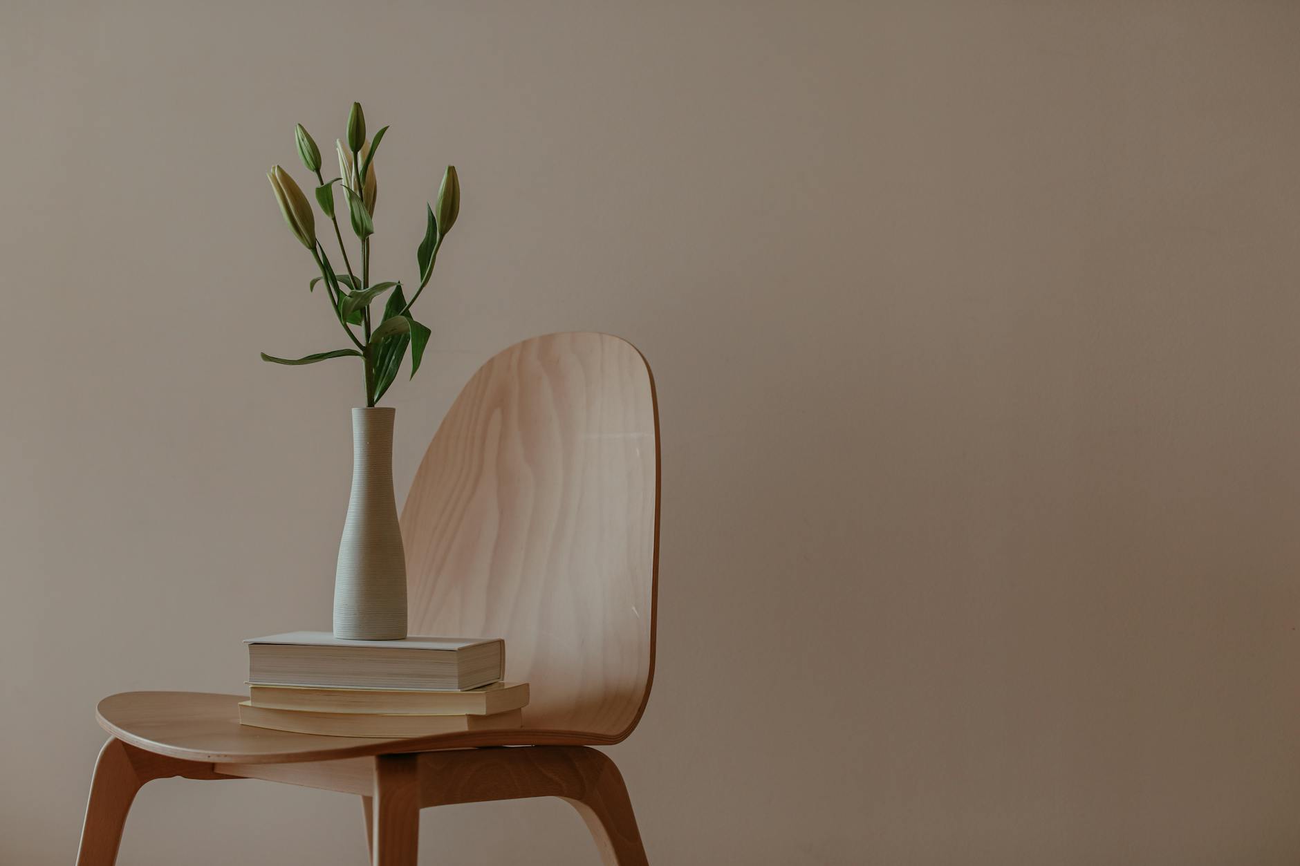 A minimalist wooden chair with a stack of books beside a window, warm natural light, uncluttered and calm