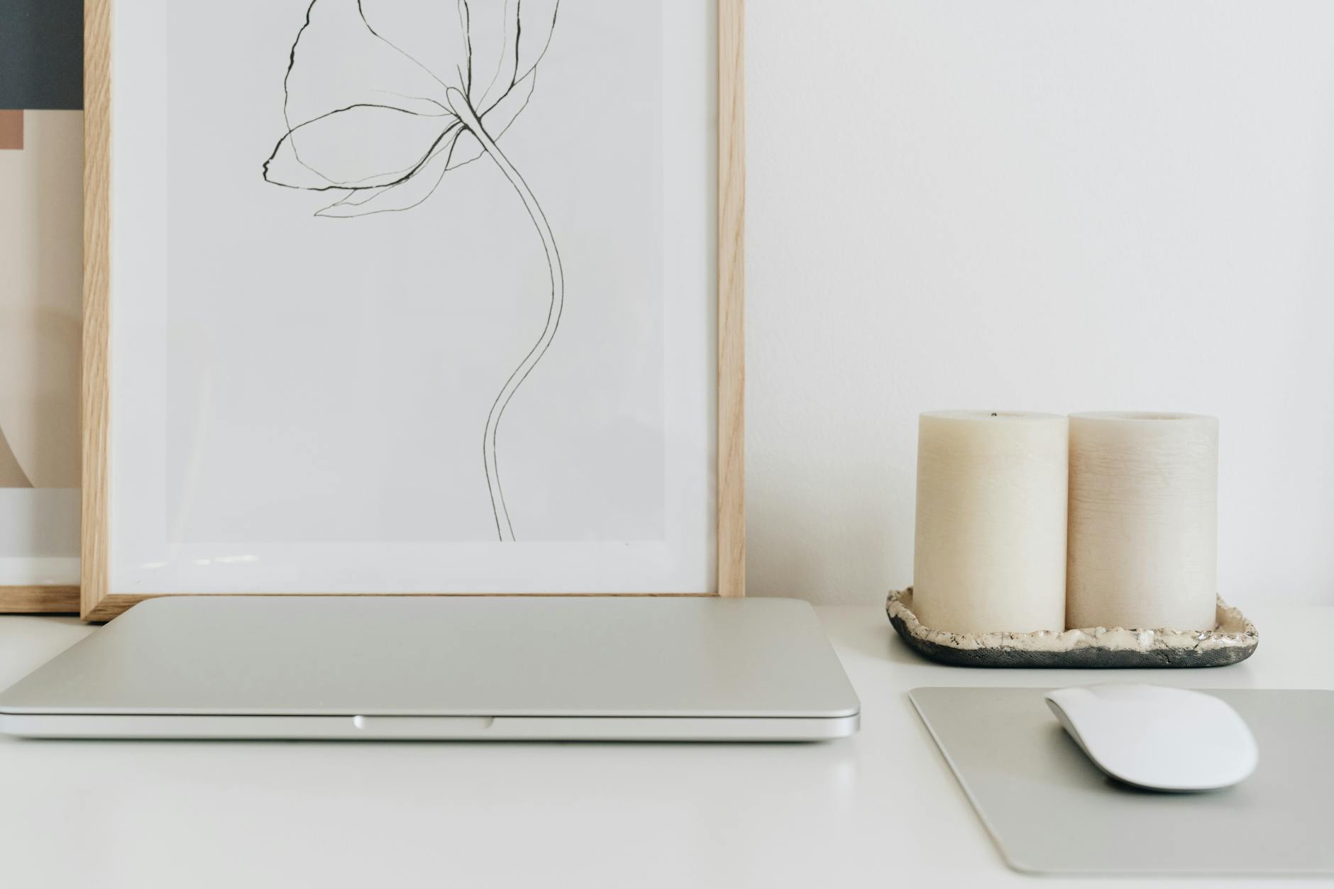 Minimalist home office setup with framed artwork, candles, and neutral tones on a white desk