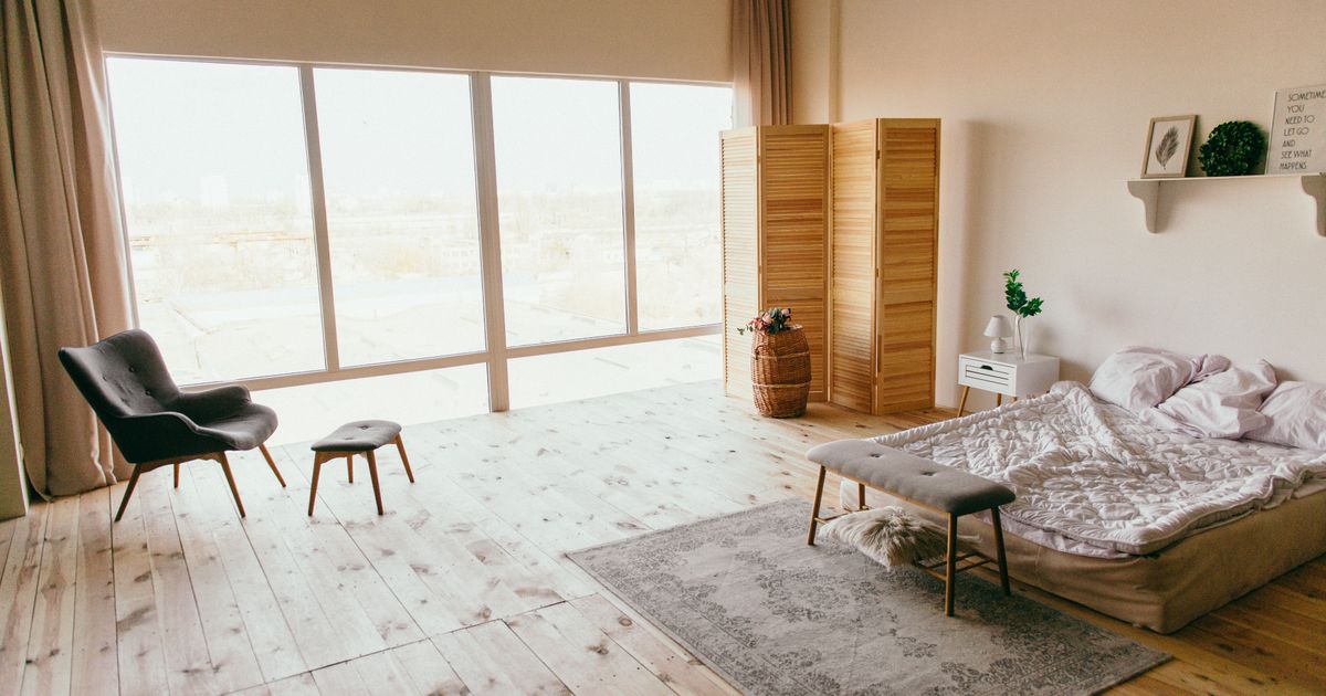 Elegant minimalist bedroom with wooden floors, large windows, and chic furniture, exuding a warm, inviting ambiance.