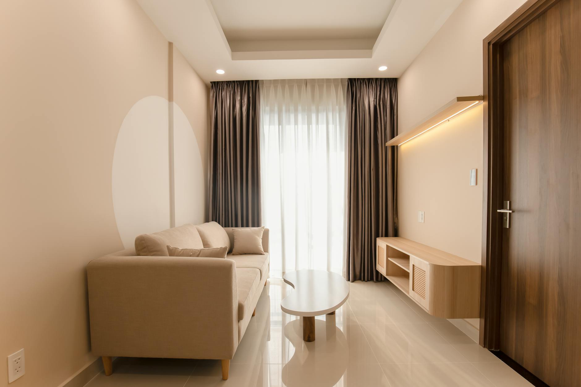 A minimalist living room with a beige sofa, warm neutral tones, and soft lighting