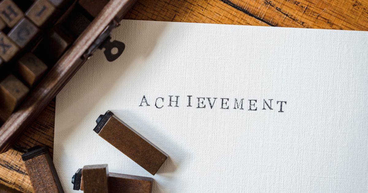 A close-up of wooden stamp typography creating the word 'achievement' on white paper.