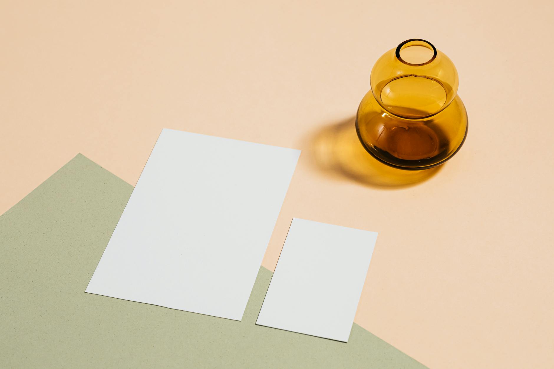 Minimalist arrangement of papers and an amber glass vase on a pastel surface