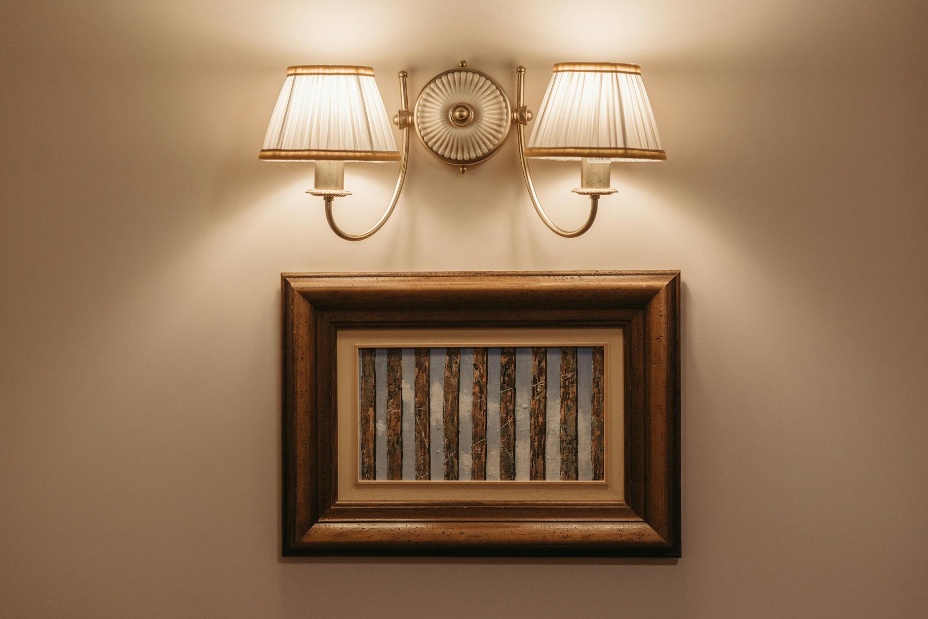 Softly lit wall lamp illuminating a framed artwork on a warm white wall, minimal composition