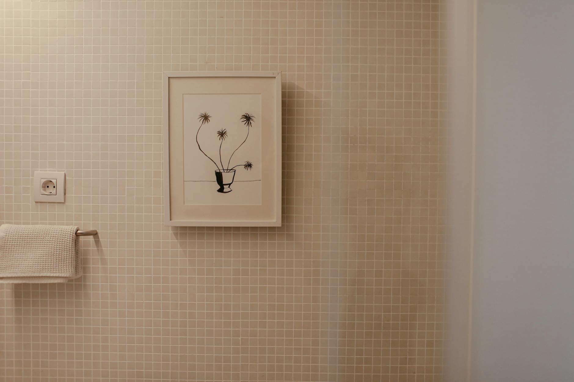 Minimal bathroom with a framed botanical print on tiled wall, warm natural light