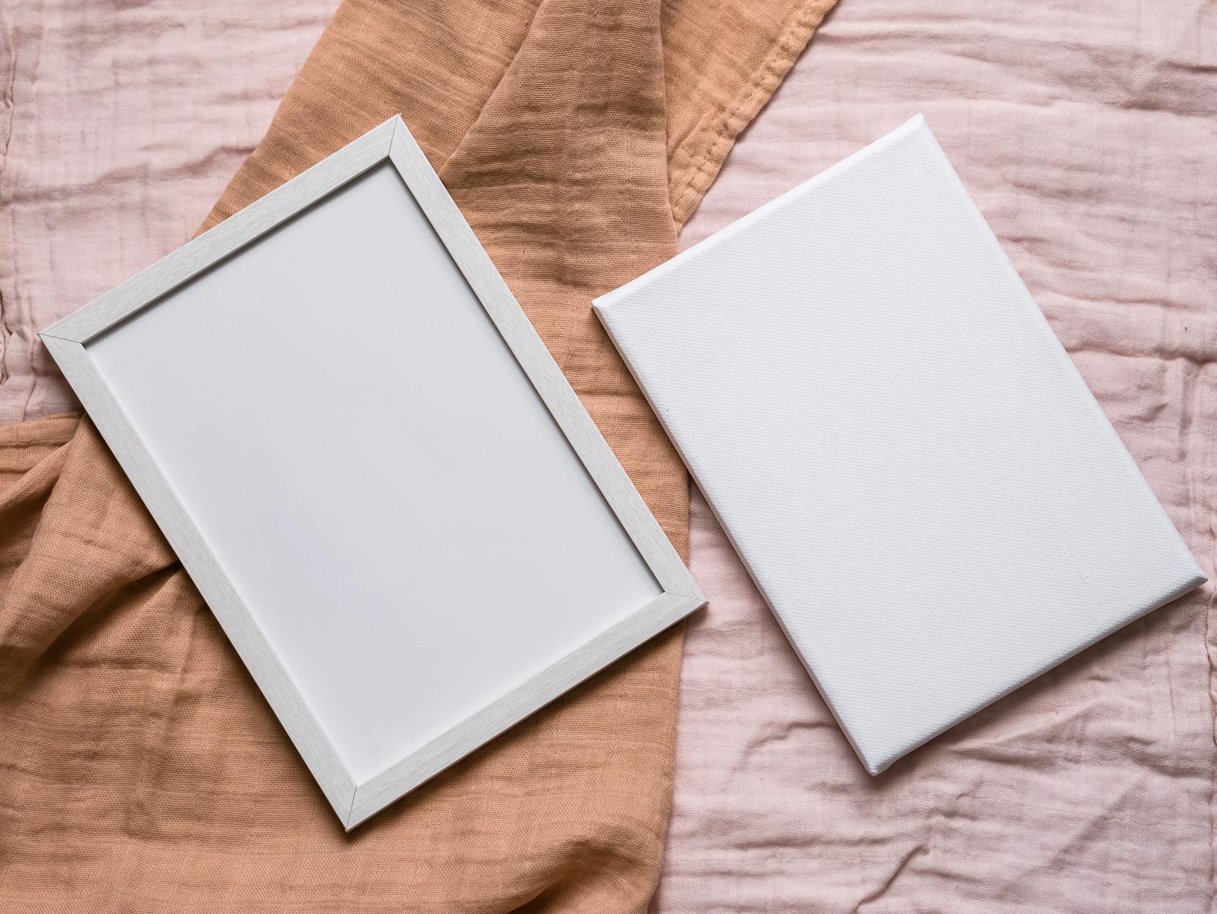 Minimalist flat lay of a photo frame and blank canvas on beige linen fabric with soft natural light